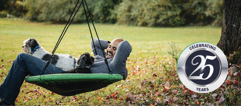 On the left a man on a swing with his two dogs and on right Malvern One Celebrating 25 years logo.